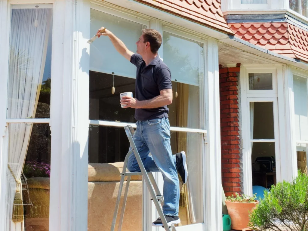 Schilder schildert een raamkozijn aan de buitenkant van een woning